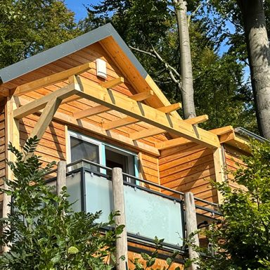 Holzhaus mit Balkon und Carport, umgeben von Bäumen.