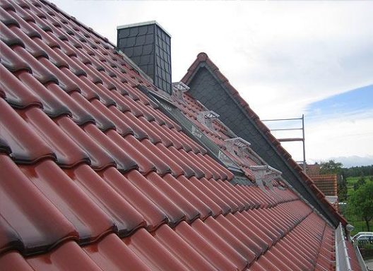 Dach mit rot glasierten Dachziegeln und mit Schiefer verkleidetem Schornstein.