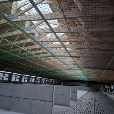 Rohbau mit Holztragwerk und Netz, große Fenster bieten Tageslicht.