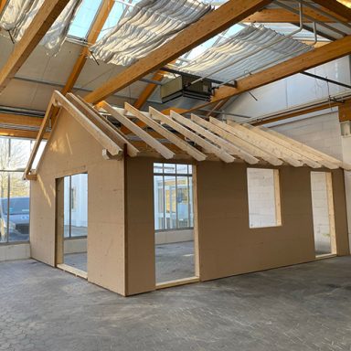 Holzbau mit Dachkonstruktion, Fensteröffnungen in einer Lagerhallenumgebung.
