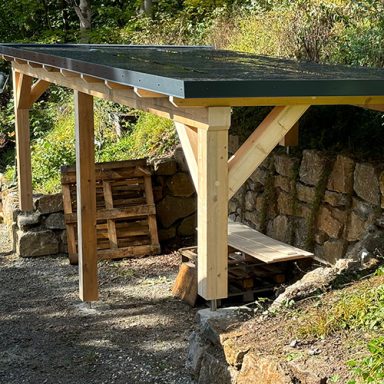 Überdachter Holzplatz aus Holz mit Paletten im Hintergrund.